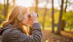 A woman birdwatcher wearing headphones and using binoculars in a peaceful forest setting during golden hour